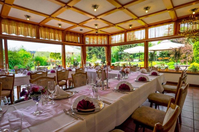 Festlich eingedeckte lange Tafel im Wintergarten mit Blick in den Garten