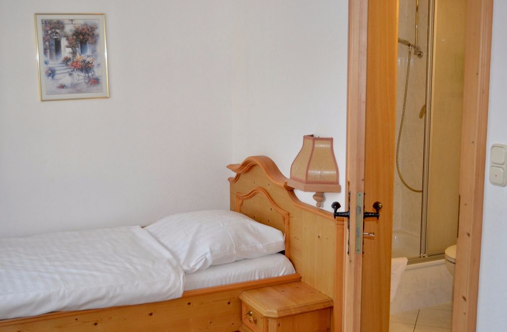 Einzelzimmer mit Holzbett und angrenzender Dusche