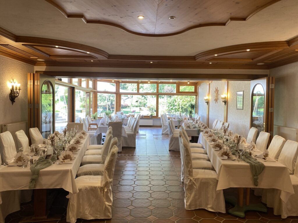 Hochzeitstafel im Saal mit weißen Stuhlhussen und Blick in den Garten