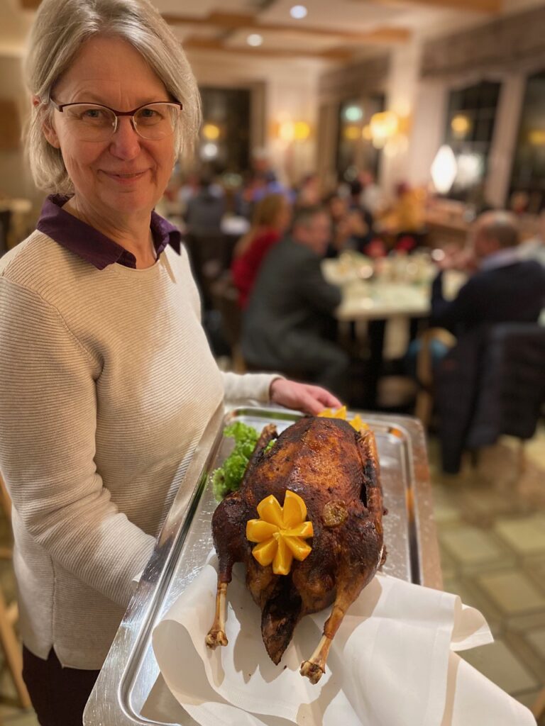 Servicekraft trägt eine ganze gebratene Gans auf einem Blech durch das Restaurant