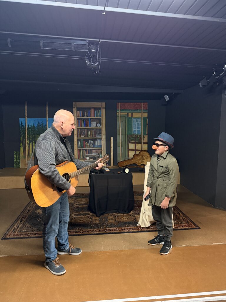 Frank Bode mit Gitarre und Detektiv Mr. Pig mit Schweinenase und Trenchcoat